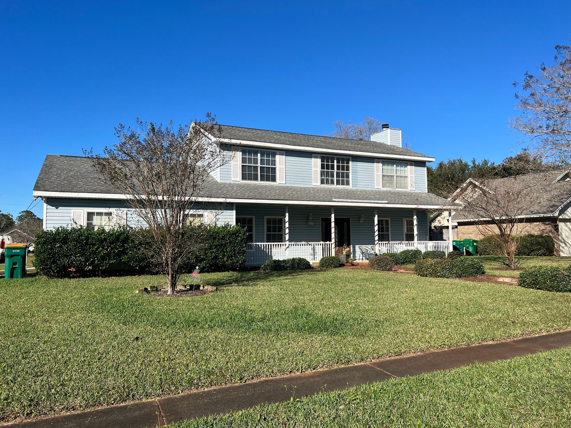 Two-story, light blue house with porch, green lawn, clear blue sky.