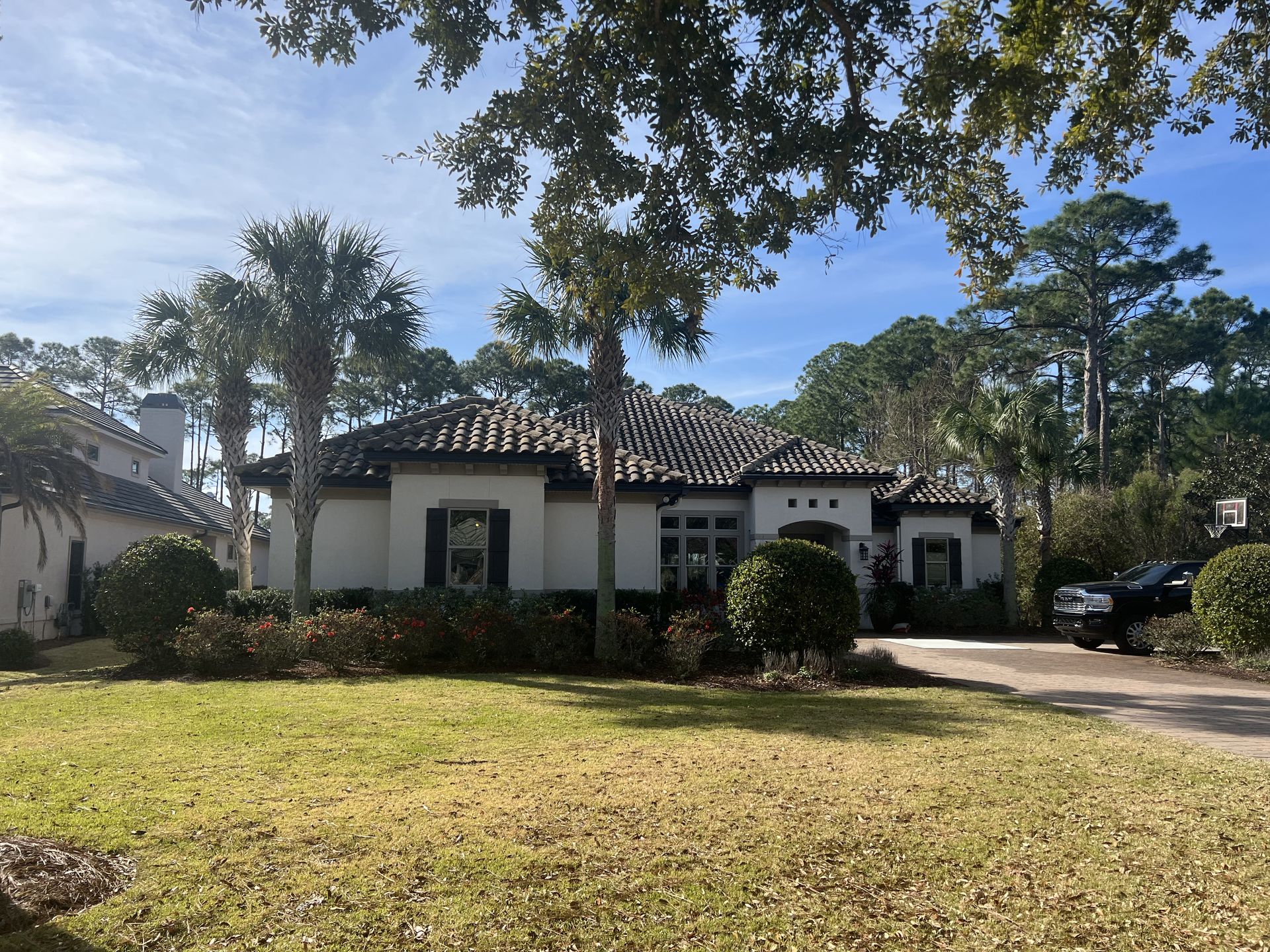 Suburban home with white exterior, dark roof, and lush landscaping on a sunny day.