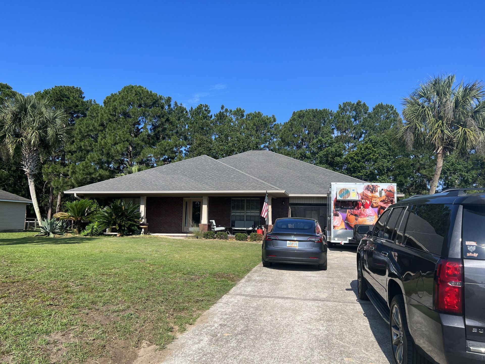 House with cars in driveway, food truck parked beside garage. Sunny day with trees in background.