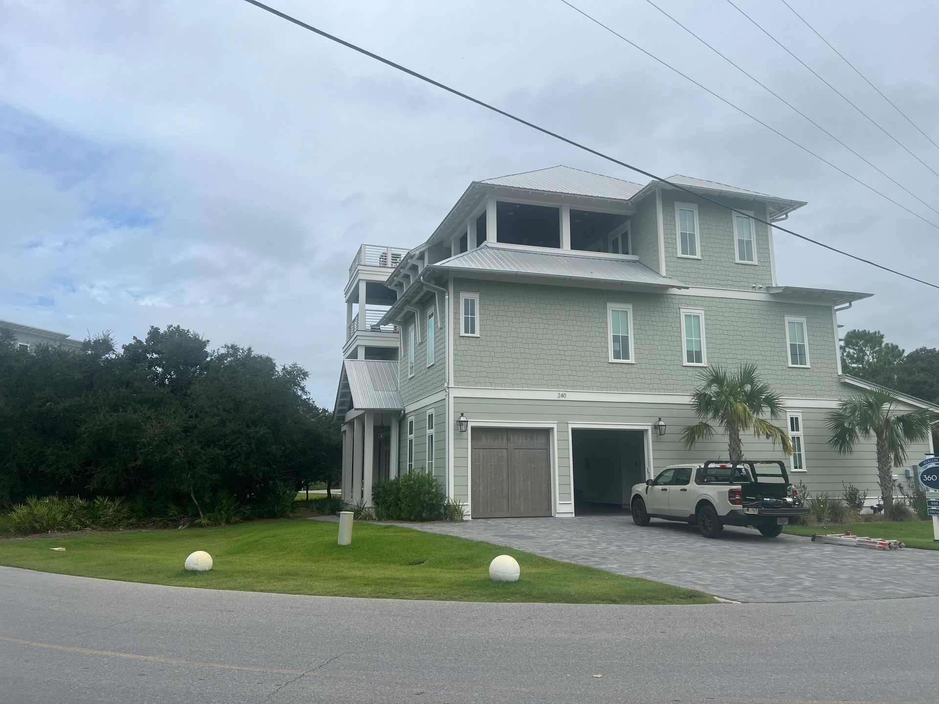 Green multi-story house with garage, driveway, and truck under overcast sky.
