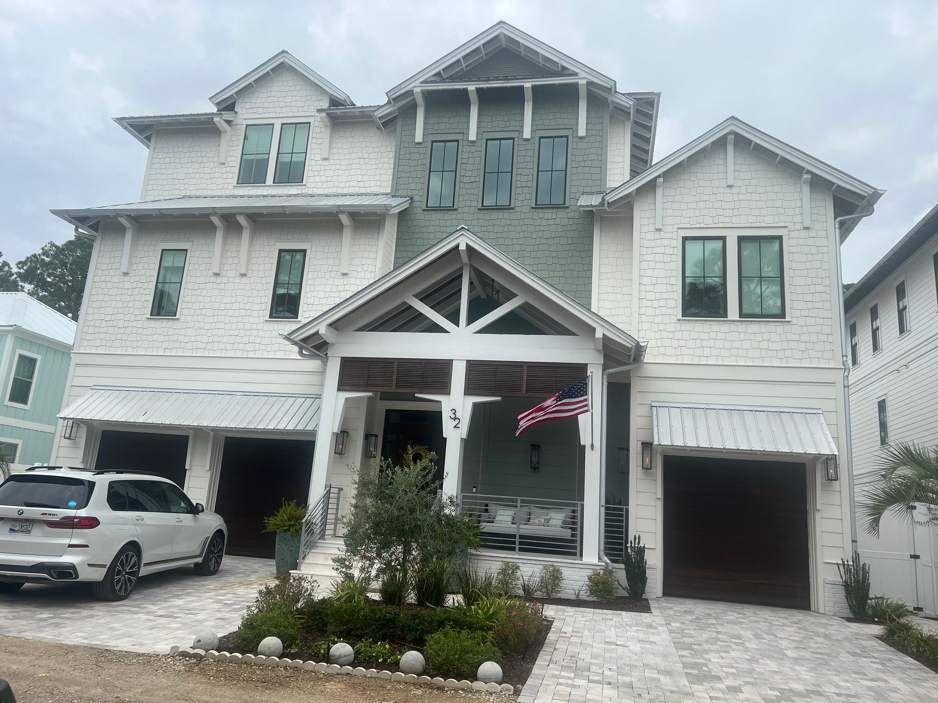 White and green multi-story house with two garages and a front porch; American flag.