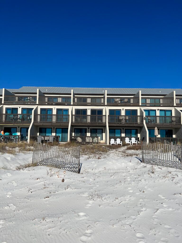 Beachfront condos with balconies, white sand, and blue sky.