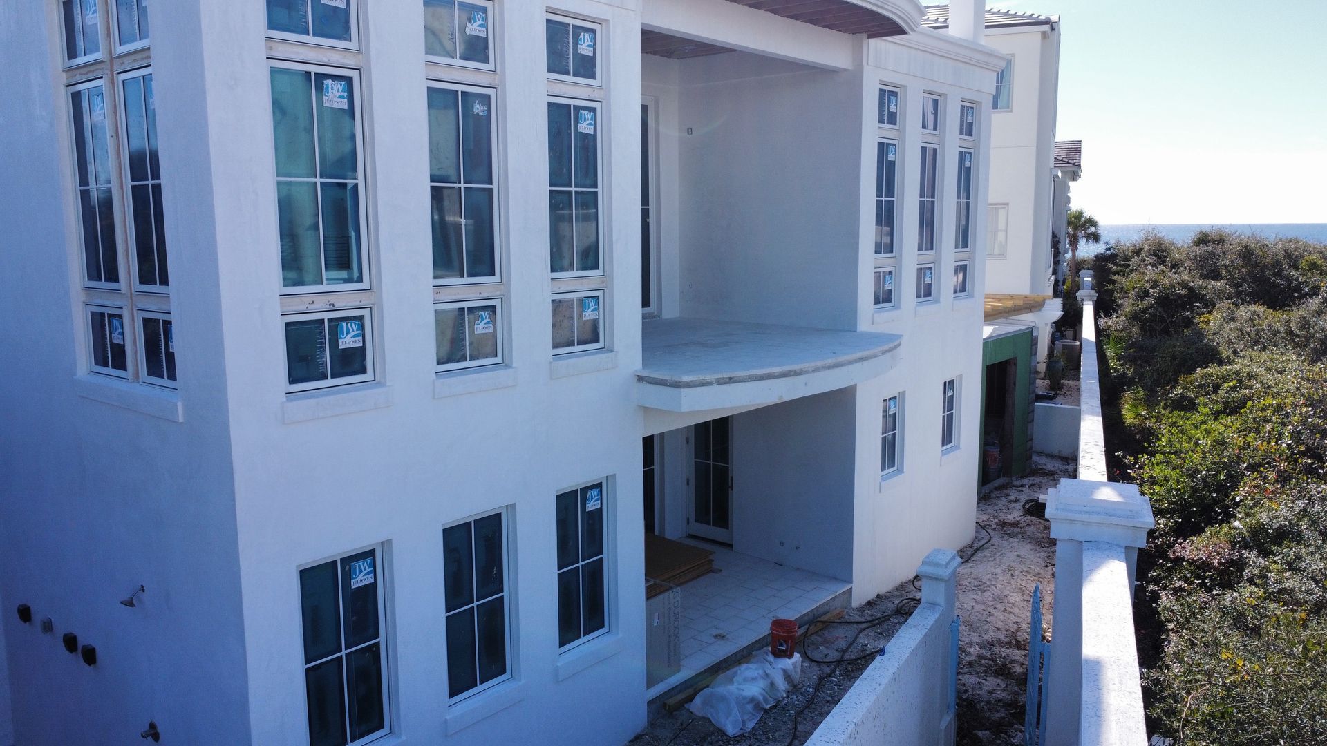 White multi-story house under construction with many windows and a balcony.