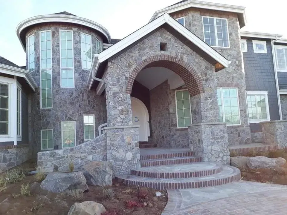 Stone-faced house with arched entryway and circular tower. Brick steps lead to the front door.