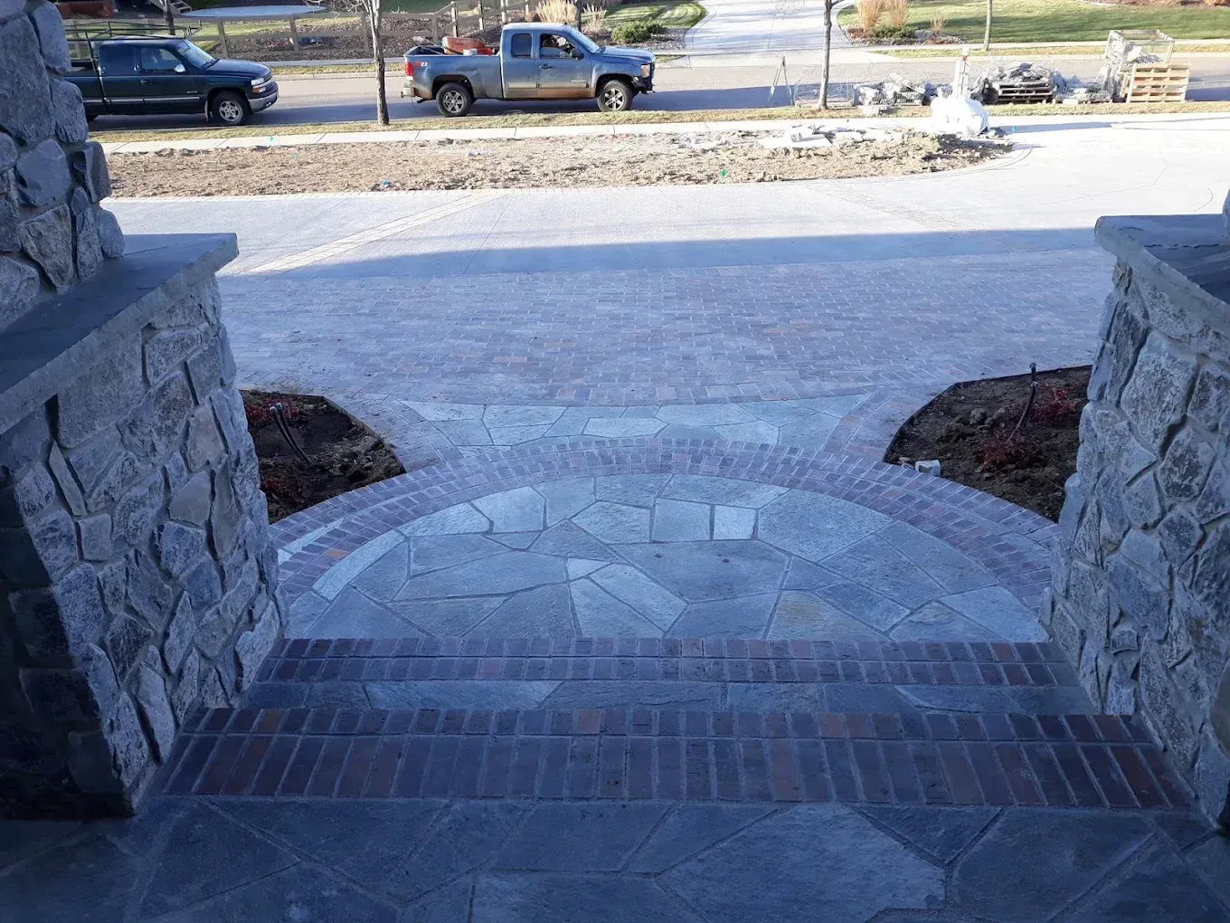 Stone steps and entryway leading to a brick and stone paved driveway with a street and cars in the background.