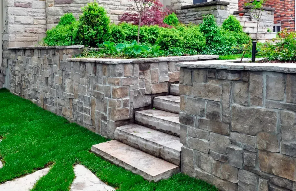 Stone retaining walls with steps leading to a garden with green shrubs and grass.