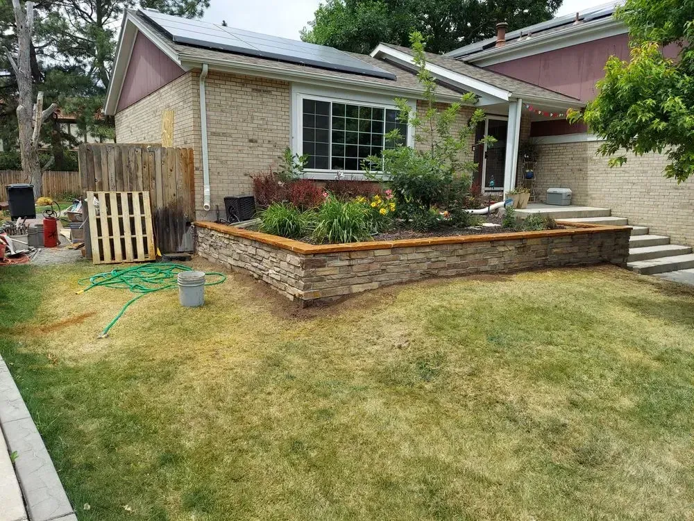 Front of house with stone-lined flower bed and steps, green grass. Solar panels on roof.