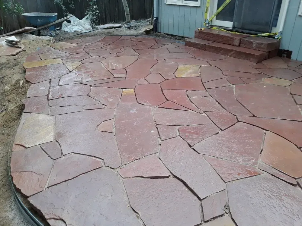 Red flagstone patio under construction with steps to a house.