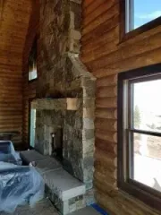 Stone fireplace with log cabin walls and windows. Interior view.