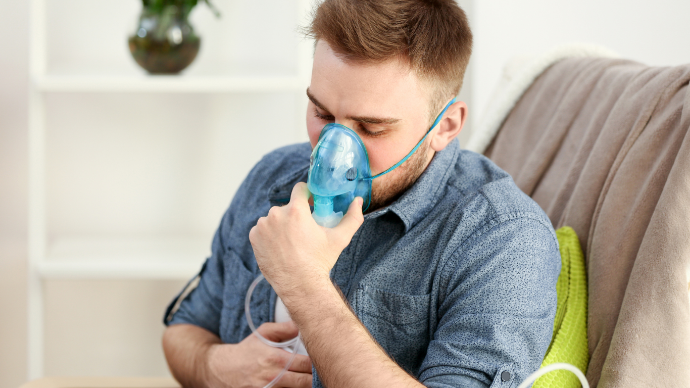 A man is wearing an oxygen mask while sitting on a couch.