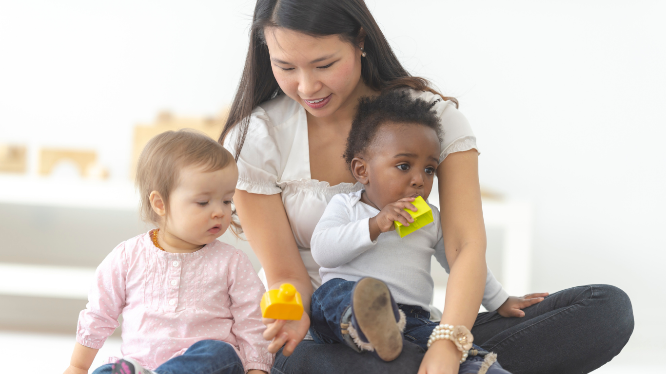 A woman is sitting on the floor with two babies.