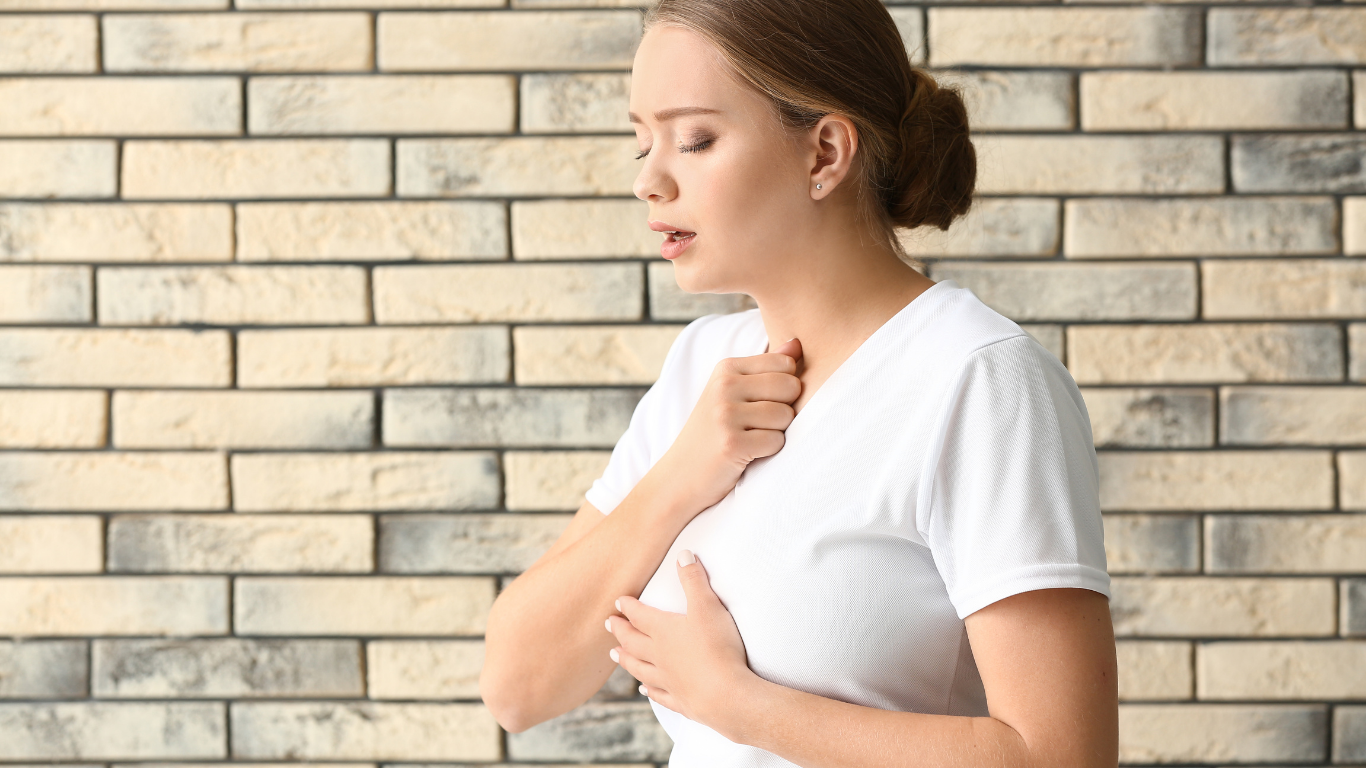 A woman is coughing in front of a brick wall.