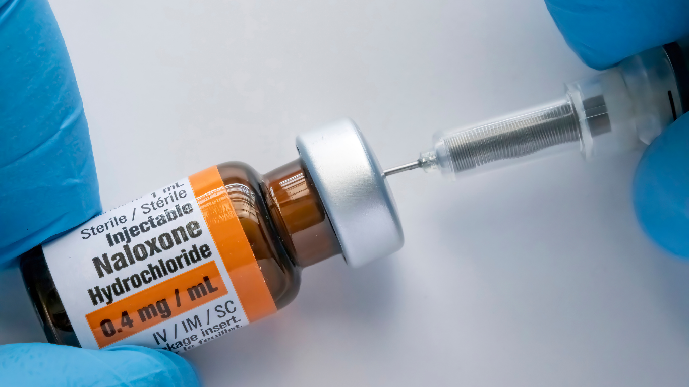 A person is holding a bottle of naloxone and a syringe.
