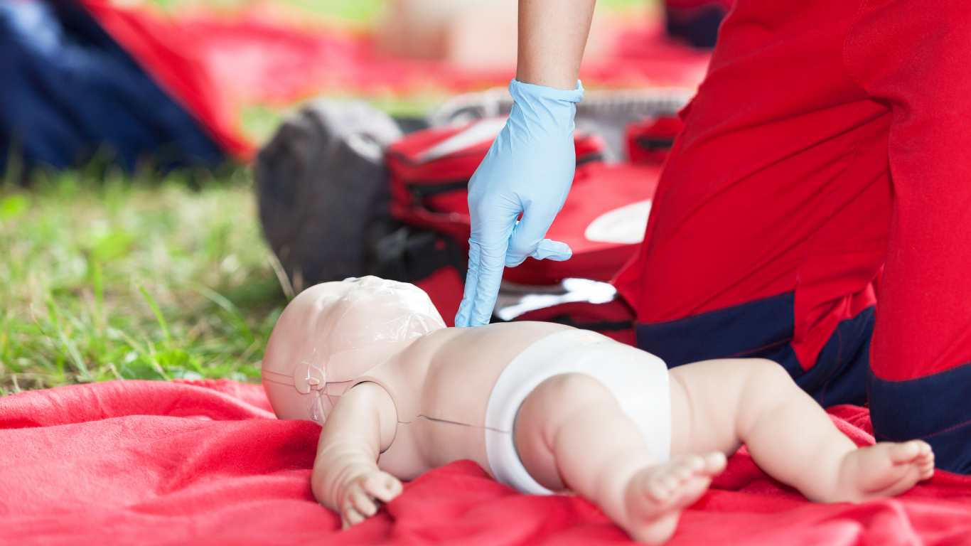A person is giving a baby a heart massage on a red blanket.