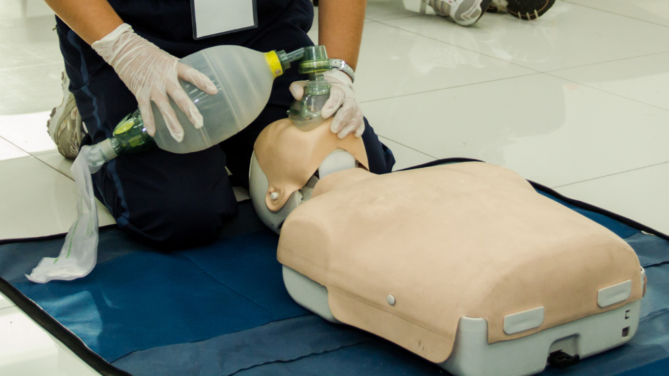 A person is kneeling down with an oxygen mask on a mannequin.