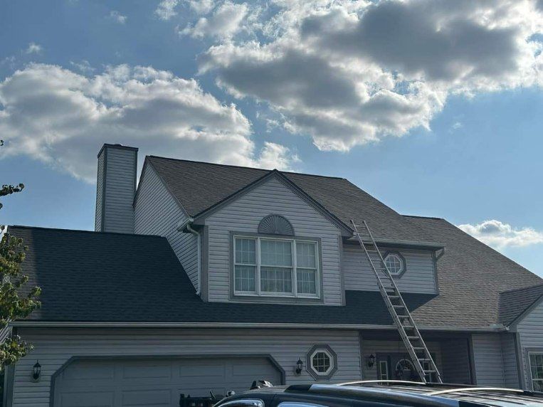 A house with a ladder on the roof and a car parked in front of it.