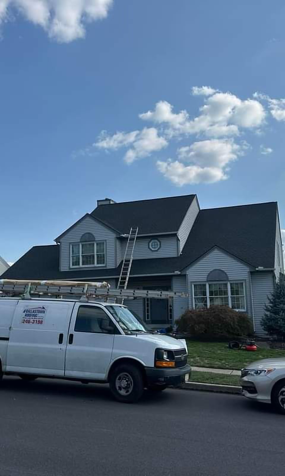 A white van is parked in front of a house with a ladder on the roof.