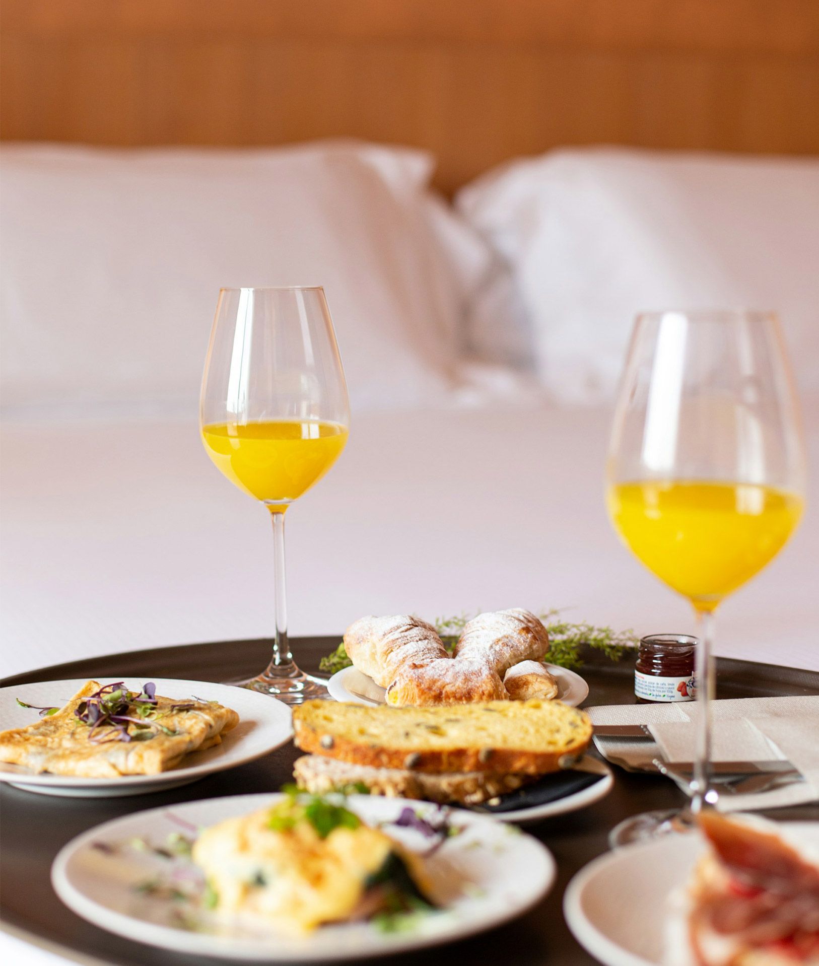 Couple holding hands, looking out a window in a hotel room, luggage beside them.