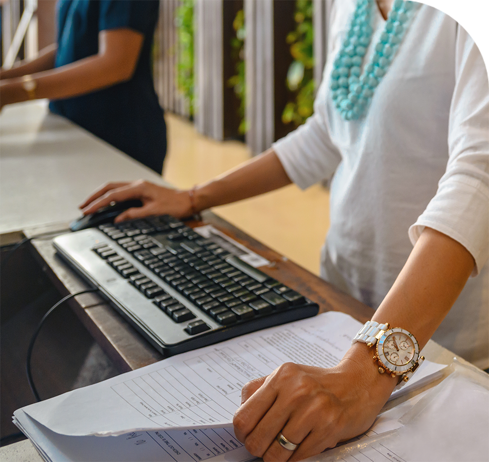 Woman at a counter with keyboard and paperwork, another person in the background.