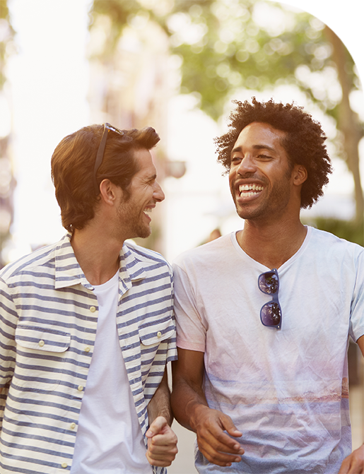 Two smiling men walking together outdoors, arm in arm. Sunny day.