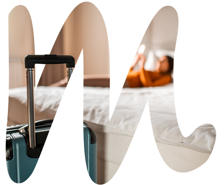 Teal suitcase next to a bed, blurred person in a room.