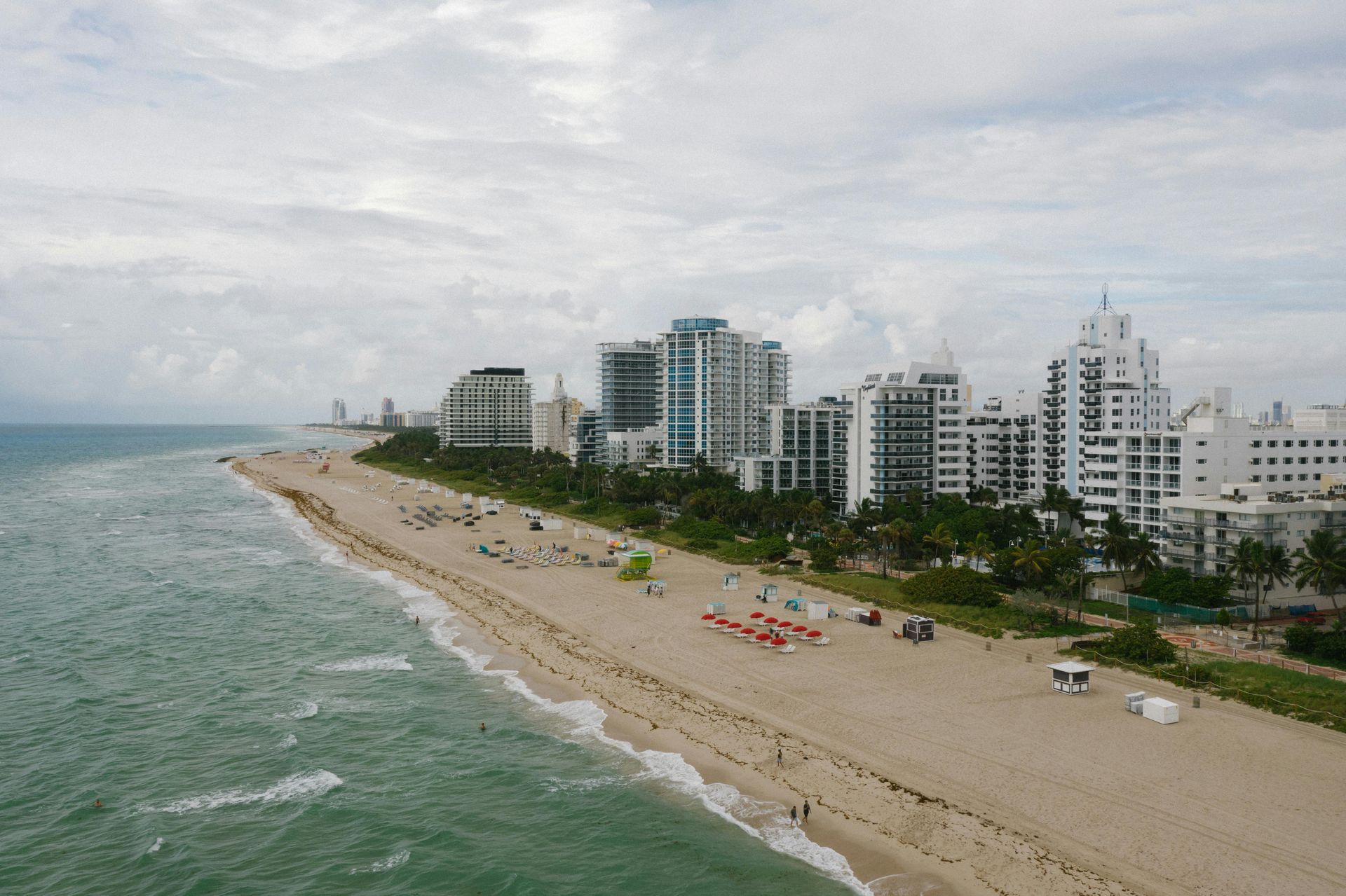 Beach and city skyline, Miami, Florida. Ocean waves, sandy shore, tall buildings, cloudy sky.