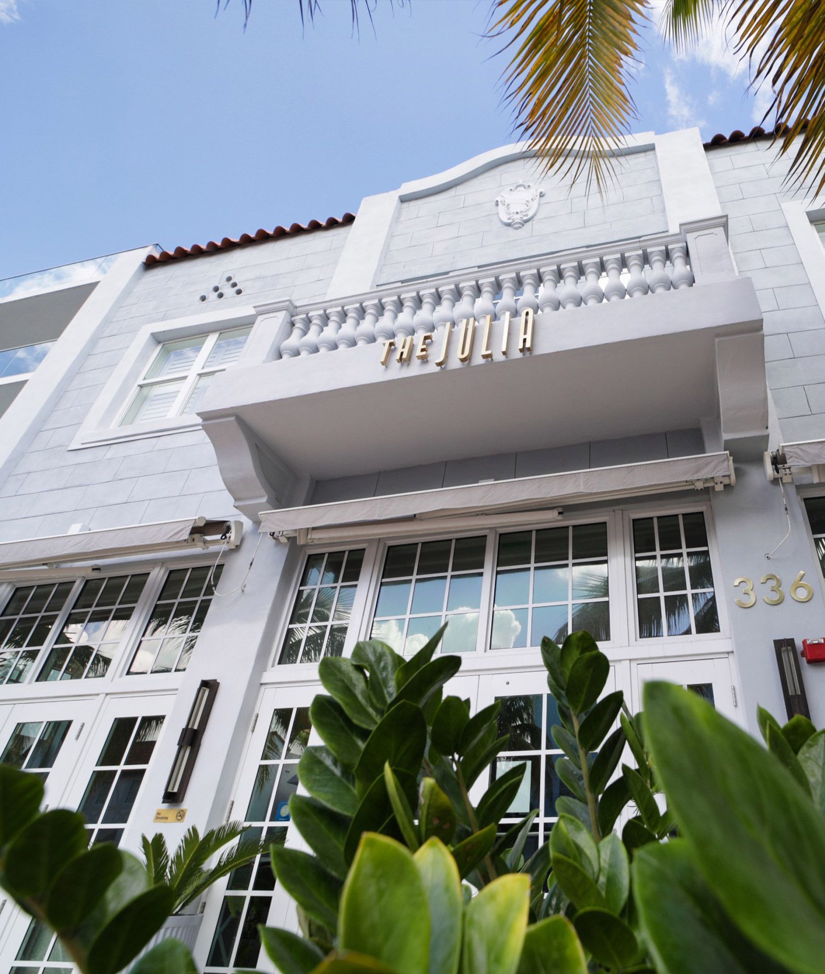 The Julia, a hotel facade with gold lettering on a balcony, framed by palm fronds.