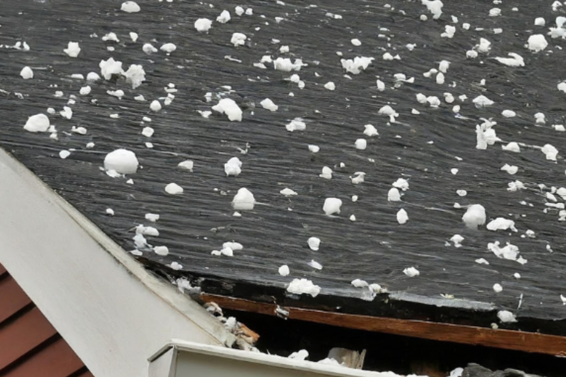 Hailstones scattered on a dark shingled roof near the edge of a house