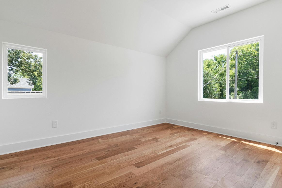 Empty room with hardwood floors, white walls, two windows, and a sloped ceiling.