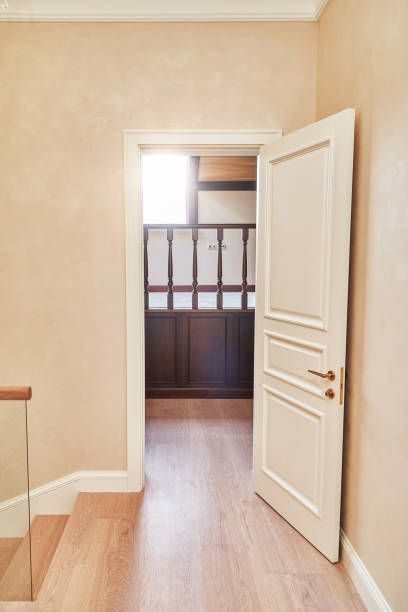A white door slightly ajar in a peach-colored hallway, leading to a dark-paneled room.