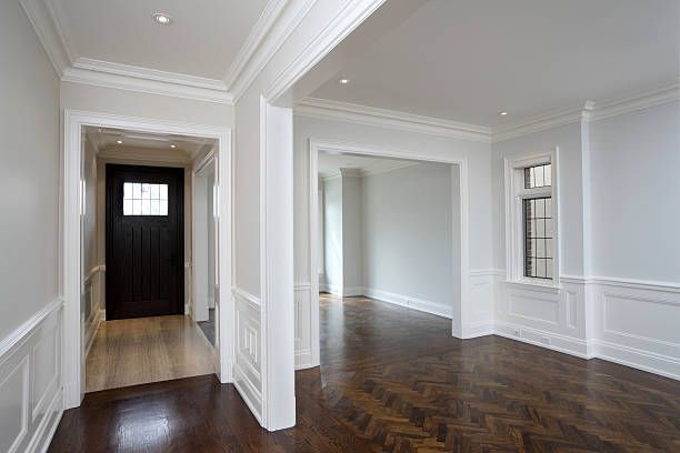 Interior with wood floors, white trim, and light gray walls. Entrance hallway with dark door, archway into a room.