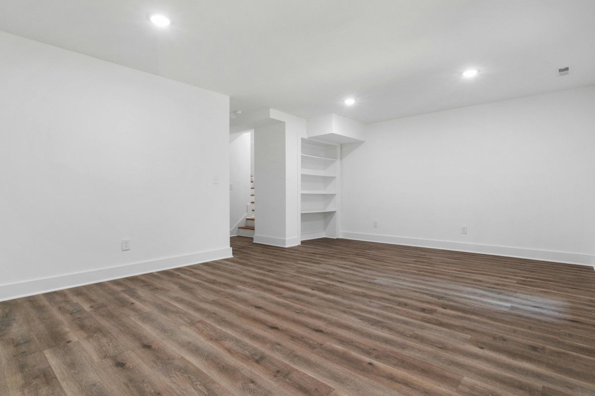 Empty room with wood-look floors, white walls, recessed lights, and built-in shelves.