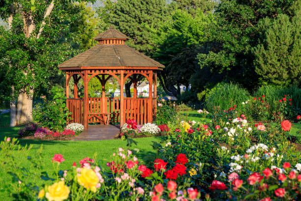 Wooden gazebo in a lush garden, surrounded by colorful roses and greenery.