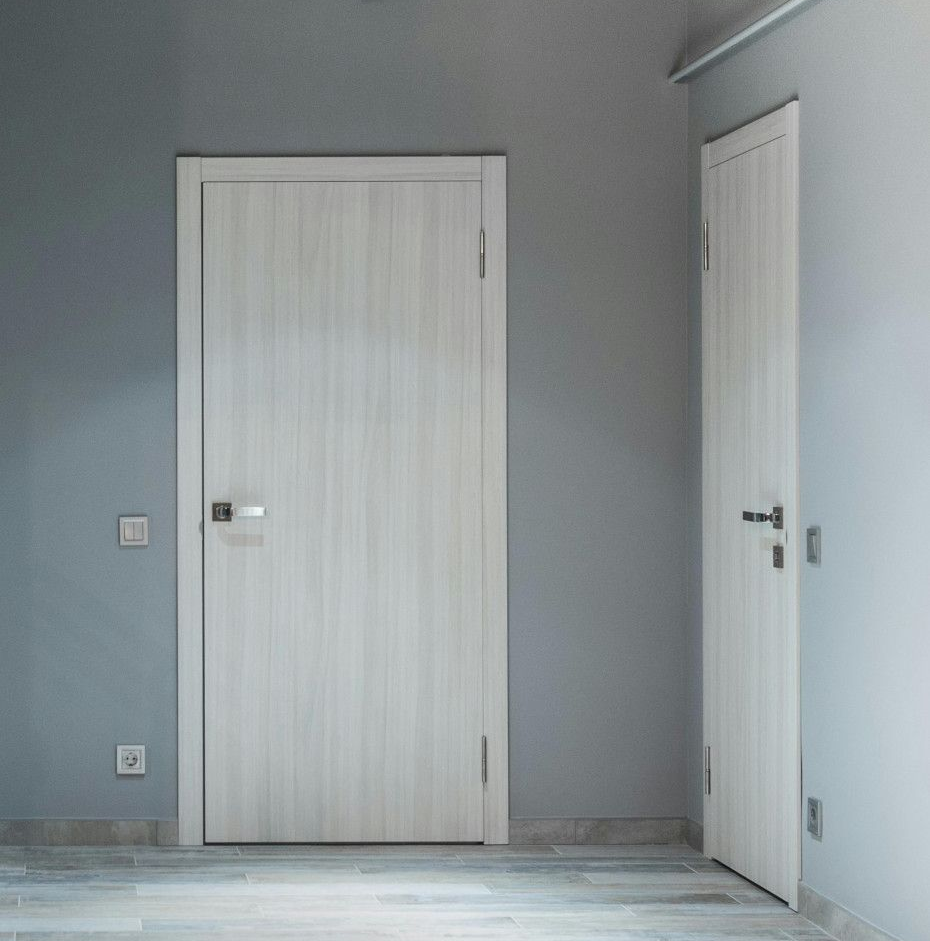 Two white doors in a room painted light blue. One is closed and centered; the other is partially open.