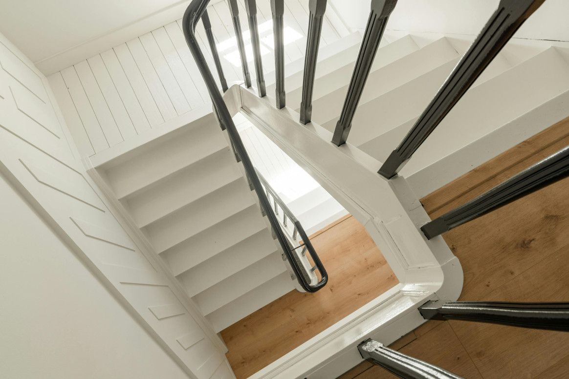 Staircase viewed from above, white steps, black railing, wood flooring, and white walls.
