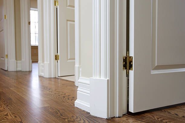Hallway with white doors, trim, and wood floors. A door is ajar, showing brass hinges.