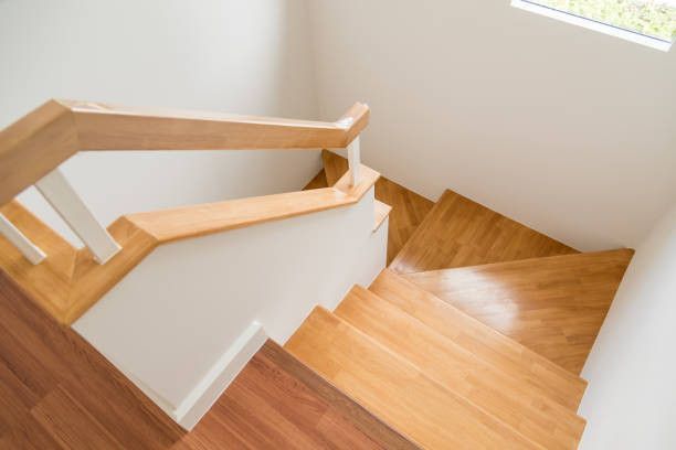 Wooden stairs descending from a white wall; wooden handrail and wood-look flooring are present.