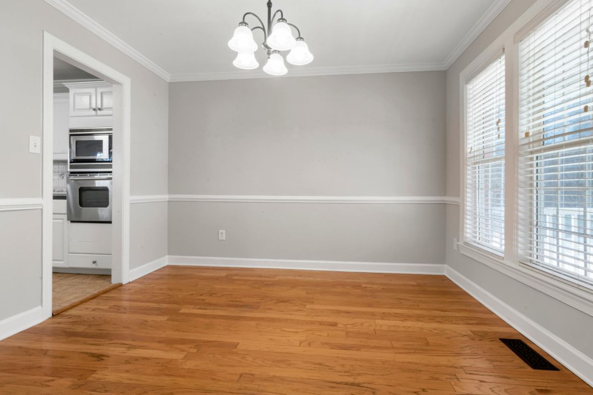 Empty dining room with wood floors, gray walls, and white trim.  A chandelier hangs from the ceiling.