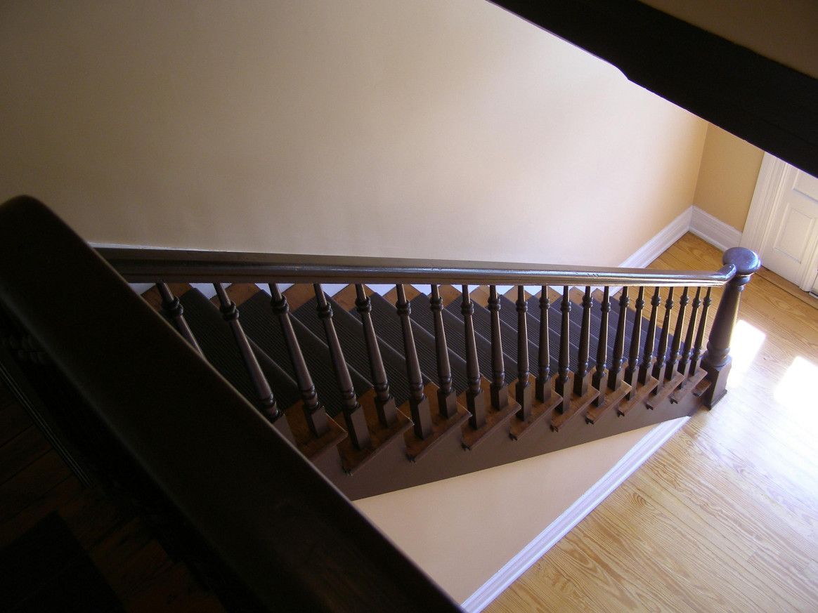 Staircase with dark wooden banister, light walls, and wooden floors.