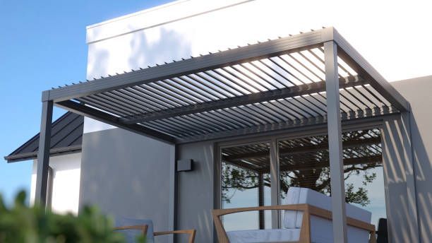 Gray pergola over patio seating against a white building, clear sky.