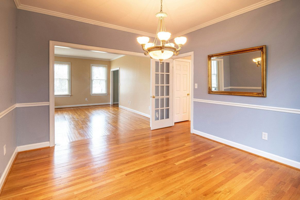 Empty dining room with light blue walls, wood floor, chandelier, and a gold framed mirror.