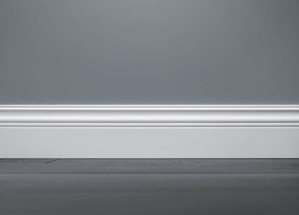 Gray wall with white decorative baseboard trim and dark floor.