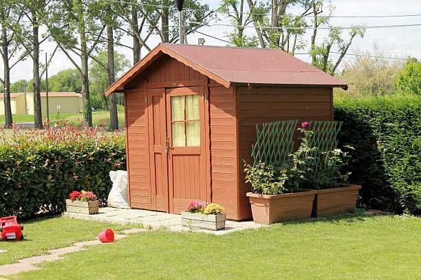 Wooden shed in a sunny garden, flanked by hedges and flower boxes; a red toy truck in the foreground.