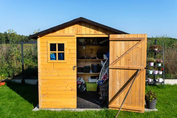 Wooden shed with an open door on a green lawn under a clear blue sky.