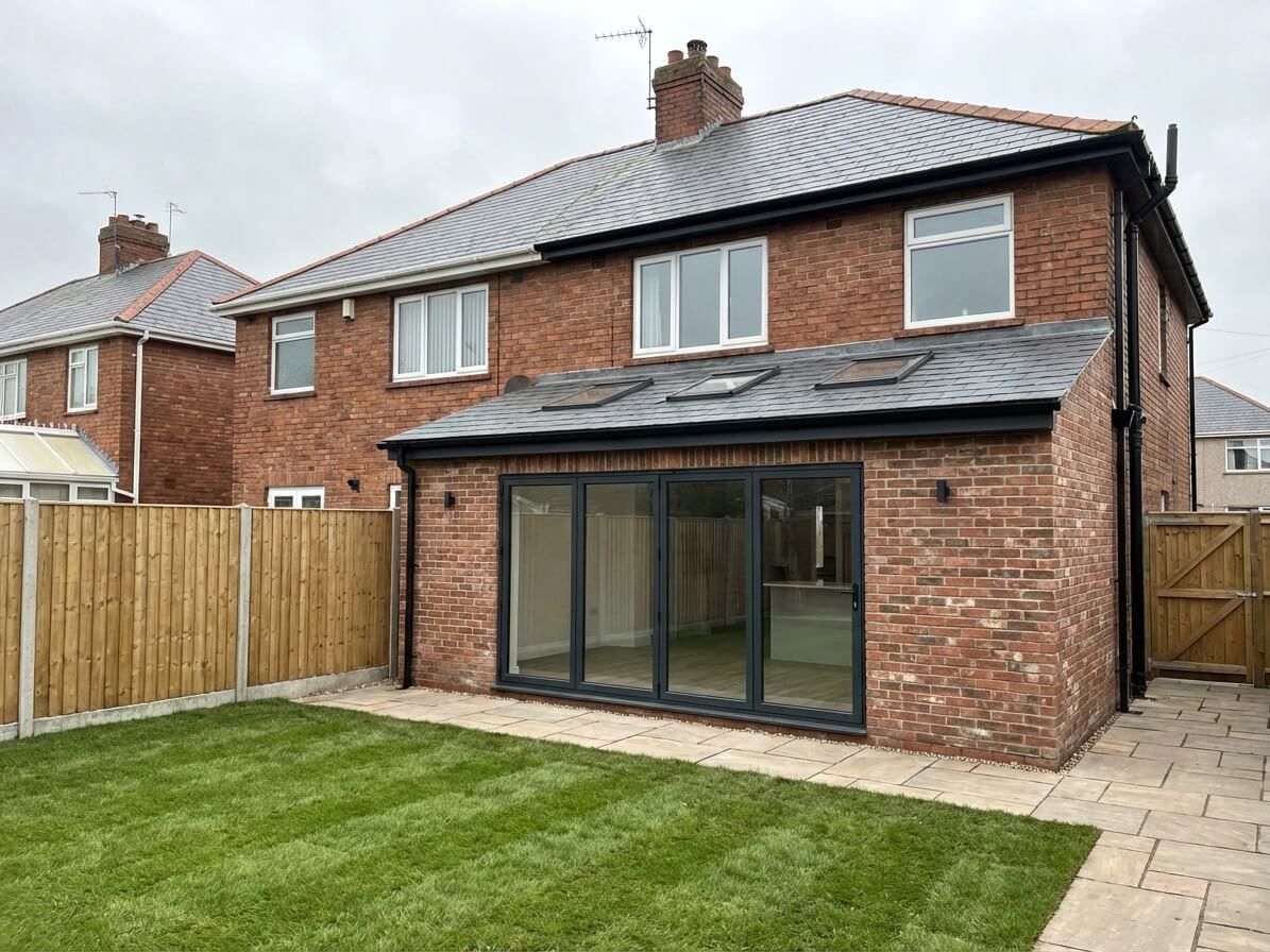 Brick house with extension, glass doors, and a green lawn in a backyard.