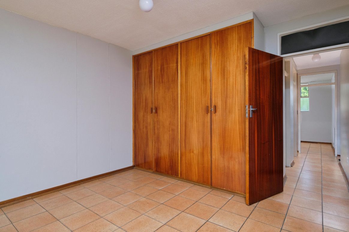 Empty bedroom with wood closet and tiled floor. Hallway visible to the right.