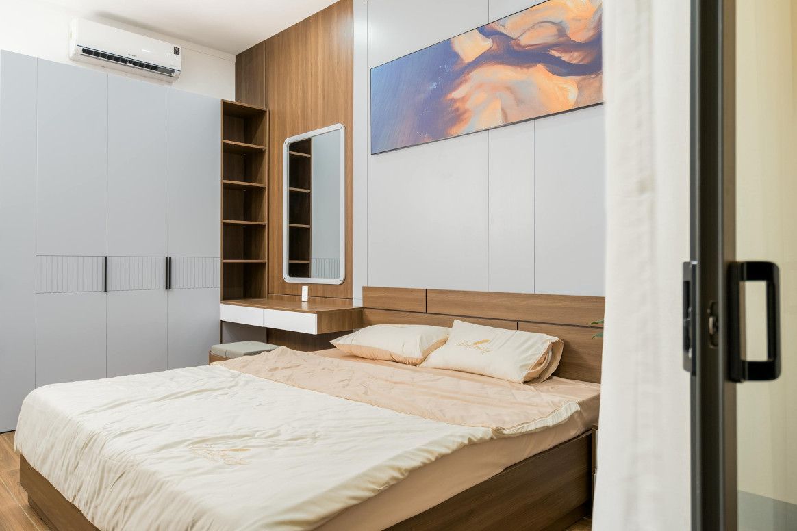 Bedroom with a bed, gray wardrobe, vanity with mirror, and an abstract painting.