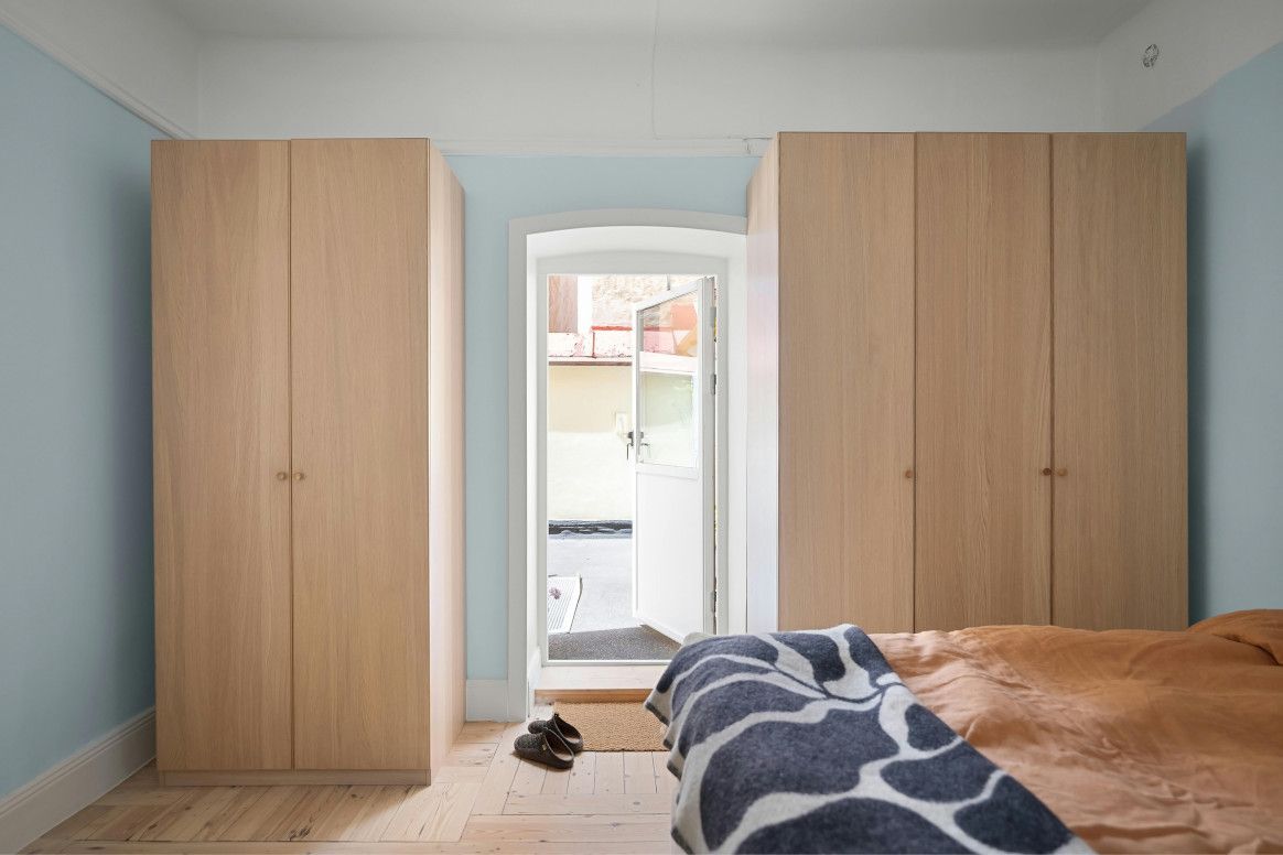 Bedroom with light-colored wood cabinets framing an open doorway. A bed with a patterned blanket is in the foreground.