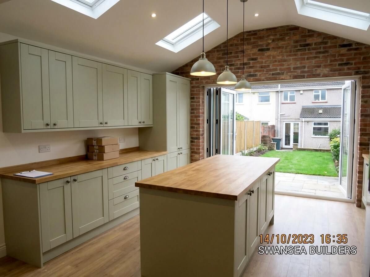 Kitchen with light green cabinets, wooden countertops, island, skylights, and a brick wall. Open to a backyard.