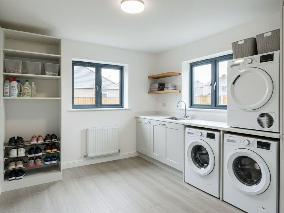 Laundry room with white appliances, cabinets, and shelving; gray windows and flooring.